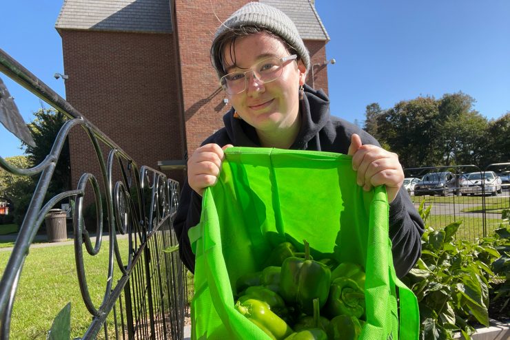 A proud student volunteer showing the bountiful harvest of bell peppers from the 依依社区 community garden.