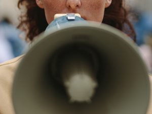 A close-up of a protestor with a bullhorn to his mouth. Behind him is a line of other protestors.