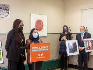 Two students, both wearing medical masks stand at the lecturn while introducing the photovoice project. A sign behind them says "Cafe Photo Voice," while a sign on the lecturn says "Emma L. Bowen Community Services Center" and includes the center's "bowencsc dot org" web address. The students are flanked by three photographs on easels. A woman and a man are at the left looking on.